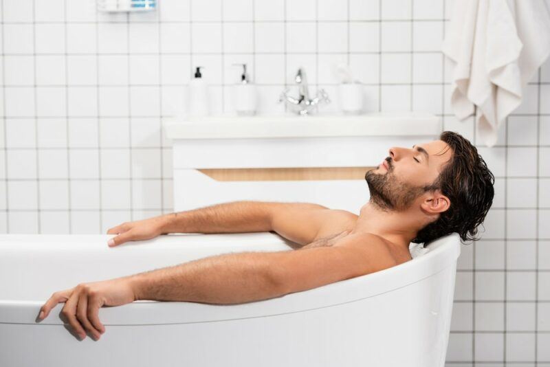 A black haired man enjoying a bath with his hands over the sides