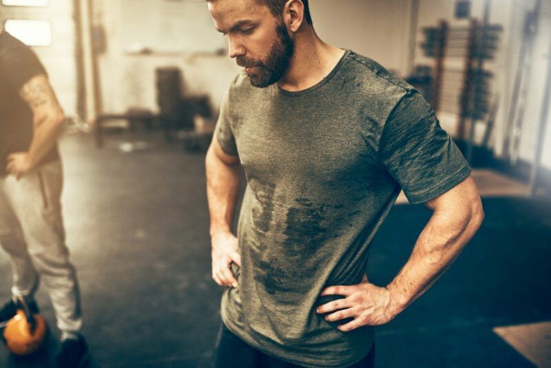 A man in a gray shirt looking down and covered in sweat