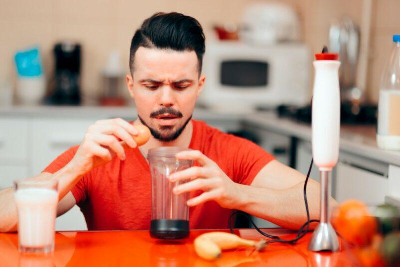 A black haired man using egg to prepare a protein shake