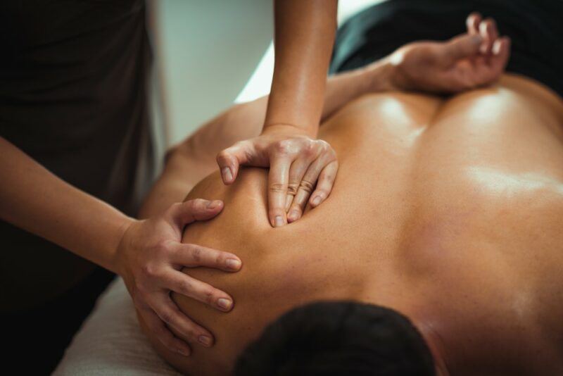 A man lying down with his shoulder being massaged