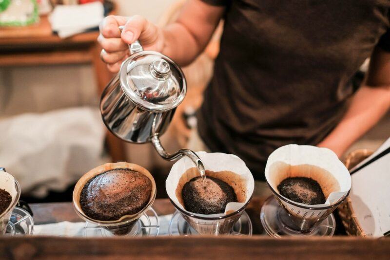 A man making three containers of filter coffee in a cafe