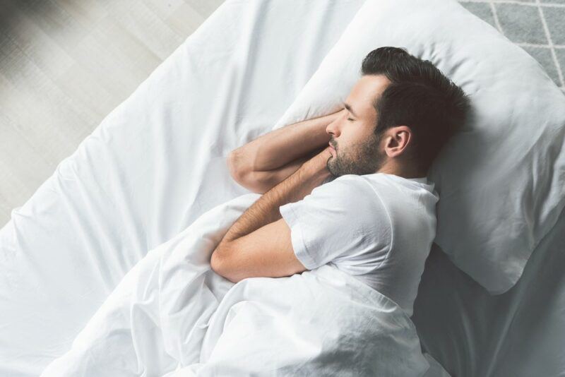 A black haired man sleeping on a bed during the day