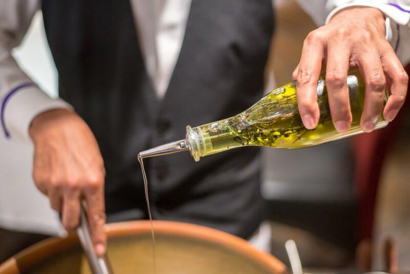 A chef pouring olive oil into a frypan for frying