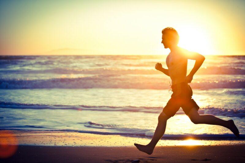 A man running on the beach with the sun setting in the background