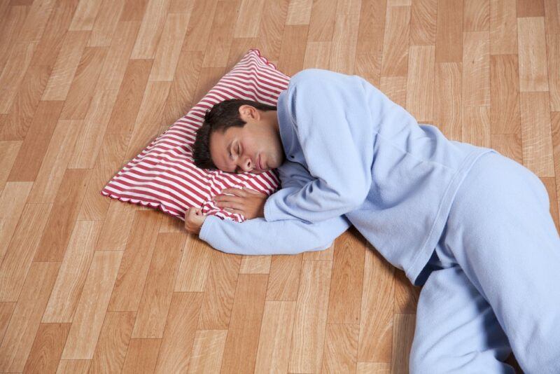 A man in blue pjs with a red pillow sleeping on the floor