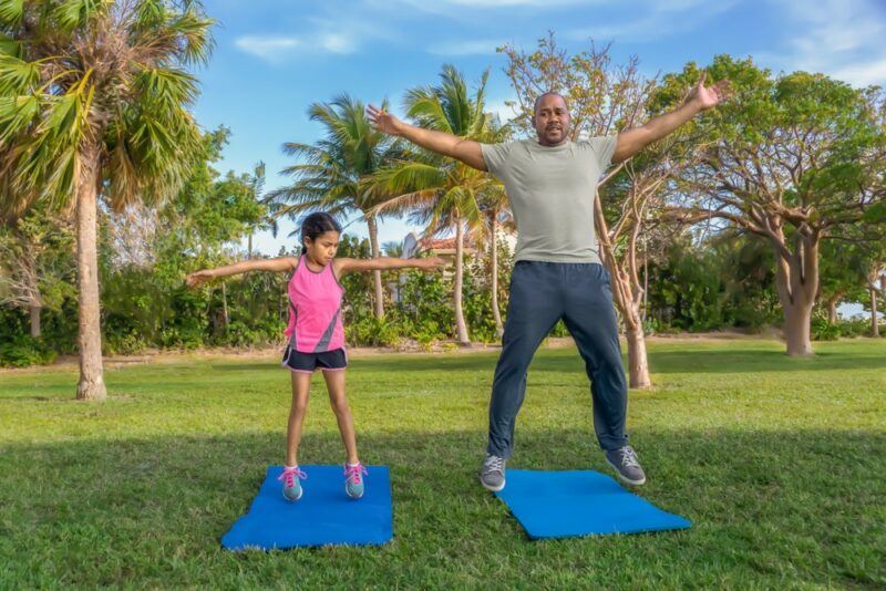 A father and daughter outside on yoga mats, practicing star jumps