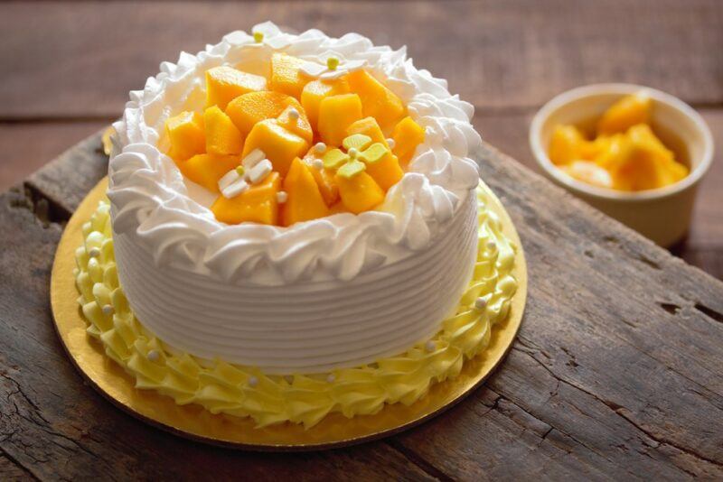 A tray with a mango, chili, and lime cake, with plenty of fresh mangos on the top