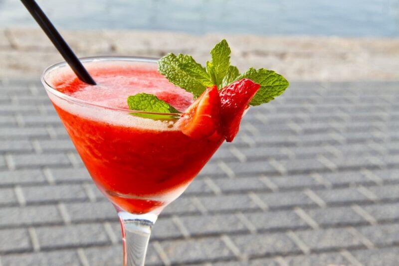 A martini glass containing a White Clas strawberry daiquiri with a straw and mint leaves