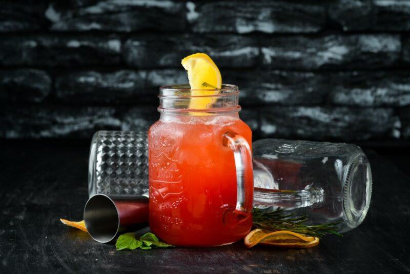 A single mason jar mug containing a tropical mountain punch cocktail with a lemon, next to plenty of bar tools