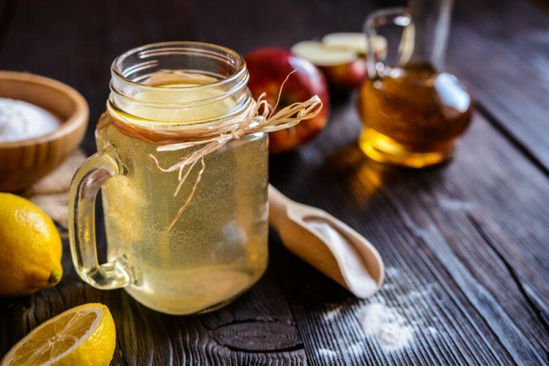 A mason jar filled with an apple cider vinegar detox drink, next to some lemons, salt, and apple cider vinegar