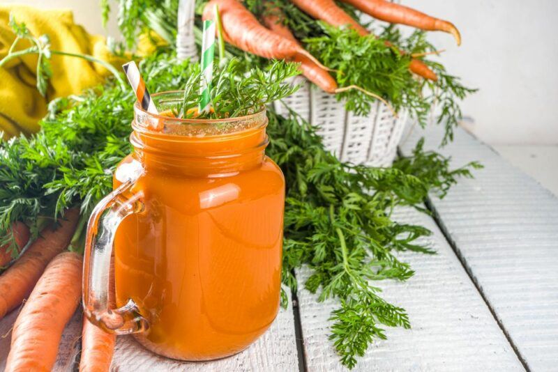 A mason jar filled with a carrot cocktail, next to carrots