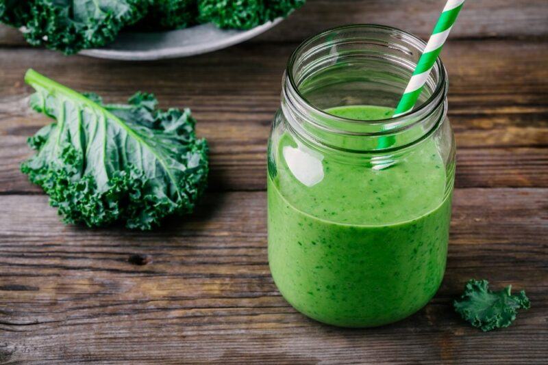 A mason jar with a kale smoothie and a straw, with curly kale on the table next to it