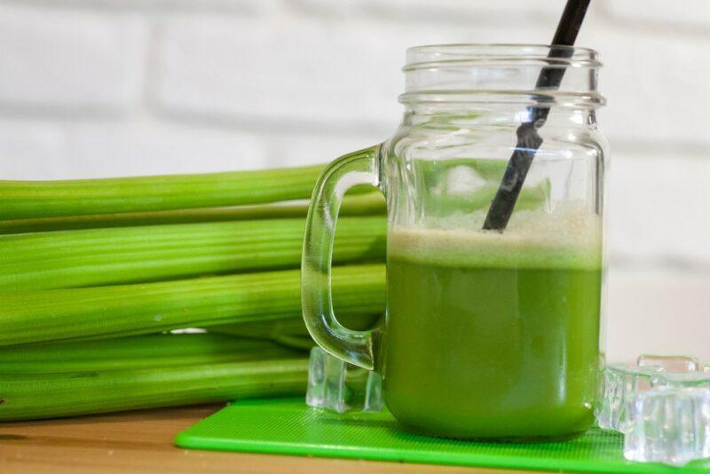 A mason jar of celery juice in front of bunches of celery