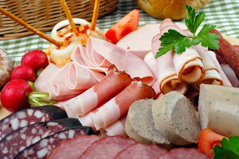 A selection of meat and cheese, with some vegetables, on a board to be served at a picnic