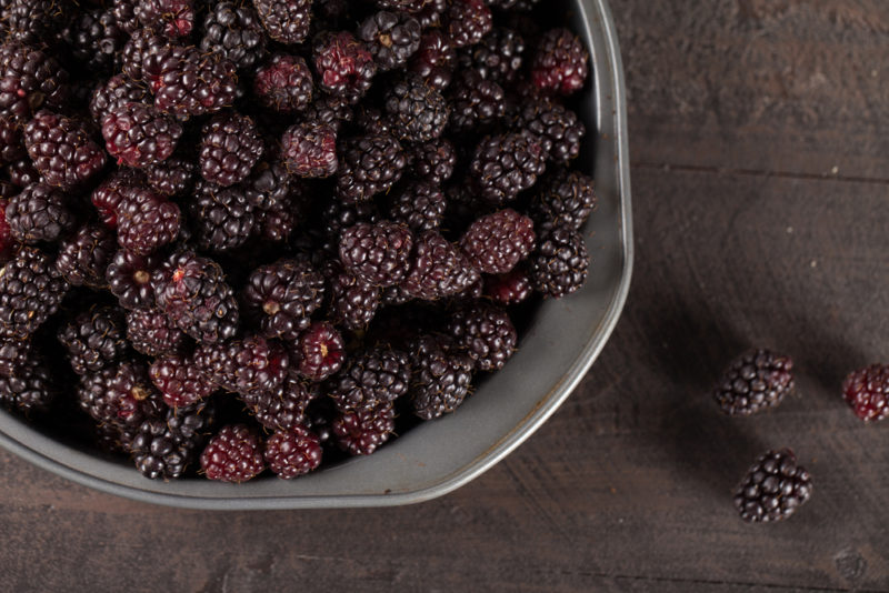 A metal dish filled with boysenberries and a few on the table