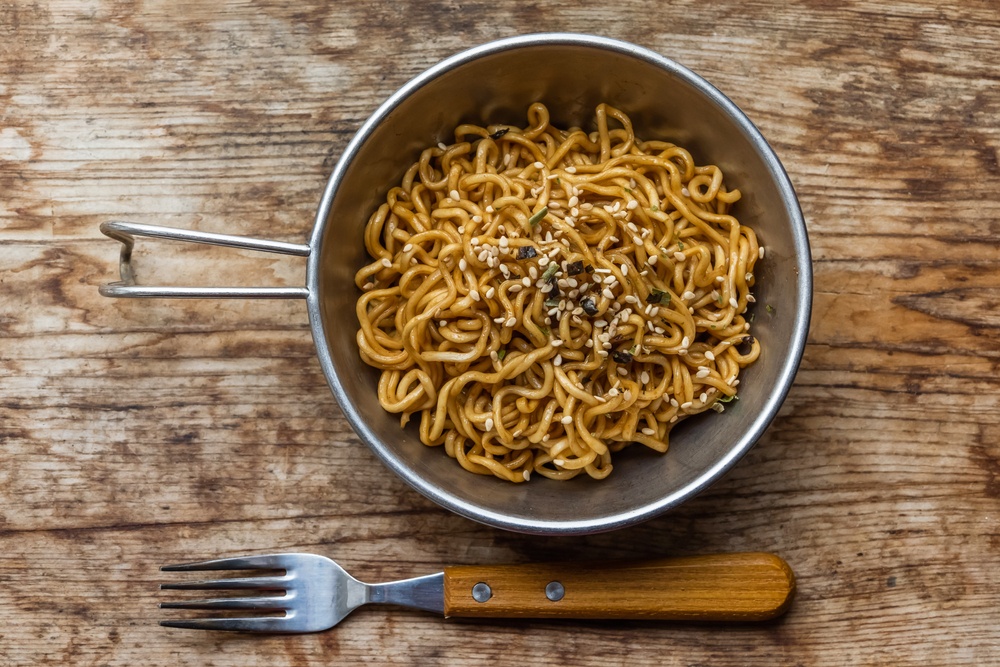 A metal bowl filled with noodles, next to a fork