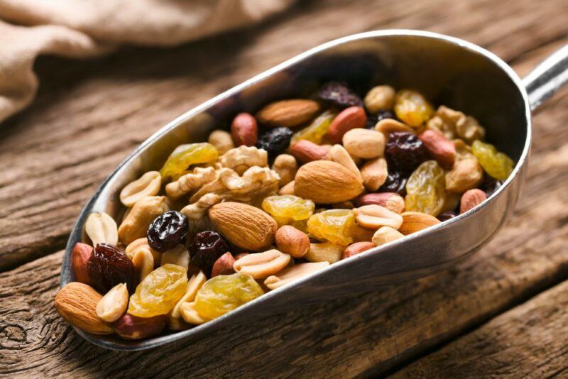 A wooden table with a large metal scoop that's filled with trail mix