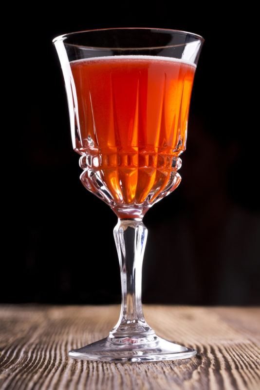 A millionaire cocktail in a crystal glass on a wooden table against a black background