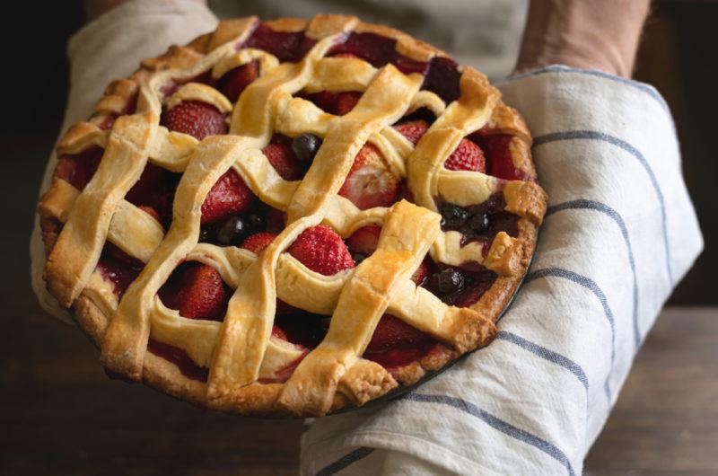 A mixed berry lattice pie being held on a striped tea towel