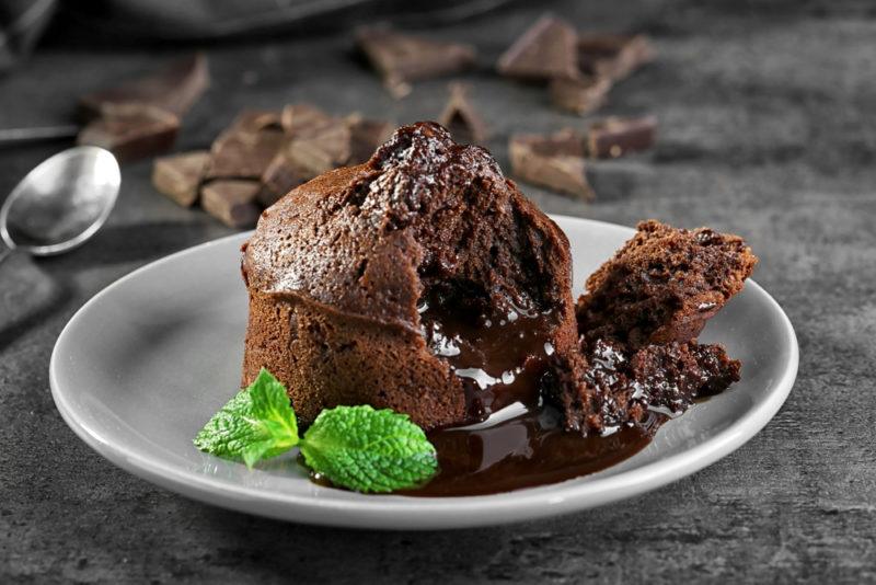 A dark chocolate lava cake on a white plate with two peppermint leaves