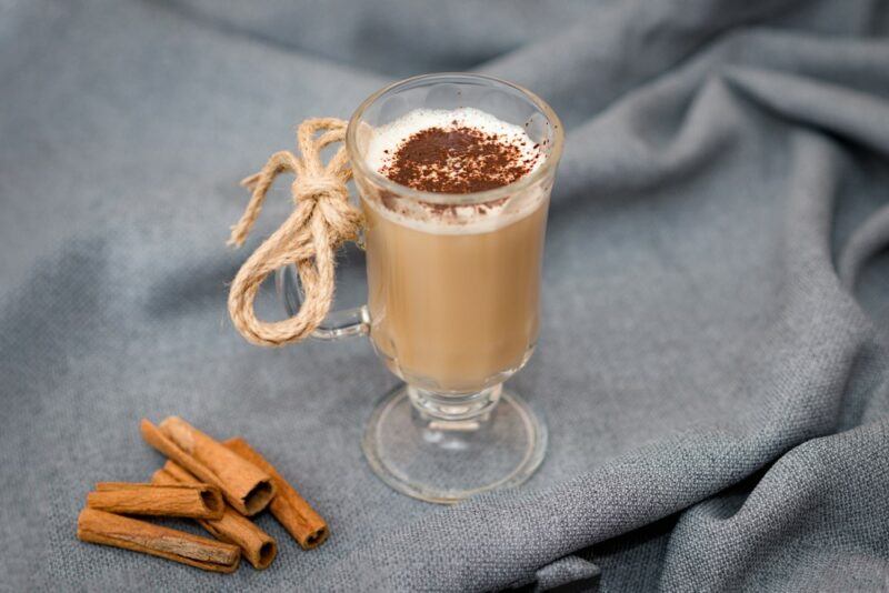 A glass mug of an eggnog latte with cinnamon sticks