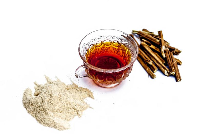 A patterned glass mug of ashwagandha tea, next to ashwagandha roots and powder