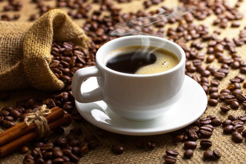 A white mug of black coffee on a pile of coffee beans, next to a bag of the beans