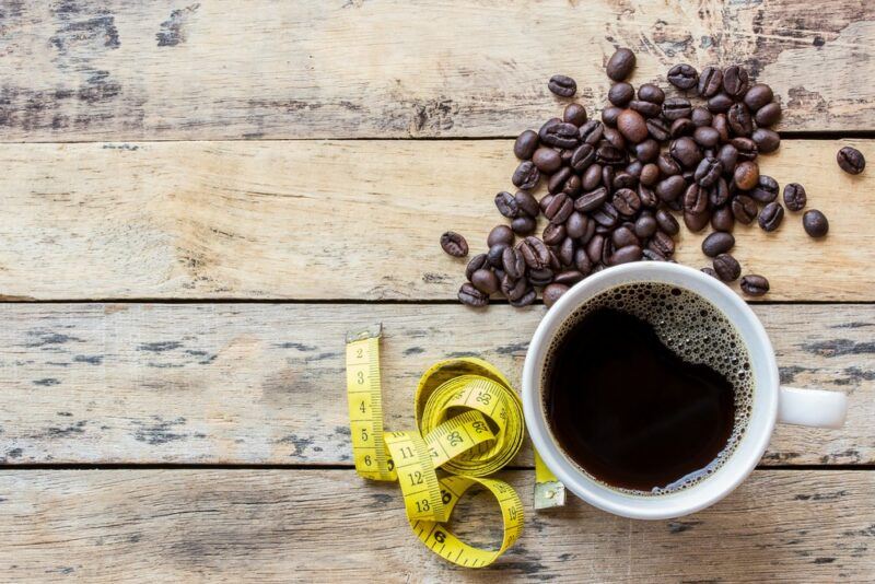 A wooden table with coffee beans, a mug of coffee, and a tape measure