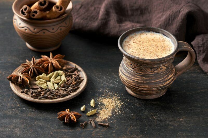 A clay mug of chai tea, next to a plate that contains all the spices used to make the tea