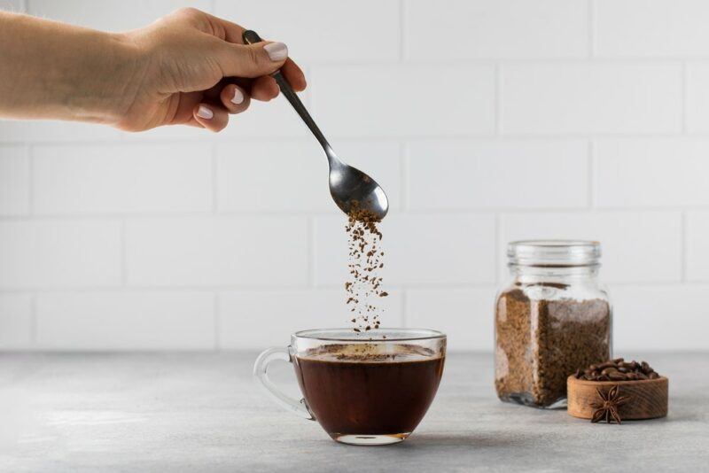 Someone making instant coffee in a mug, with a container of the coffee in the background