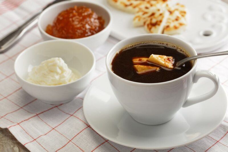 A mug of coffee next to a small bowl of cream and another of jam