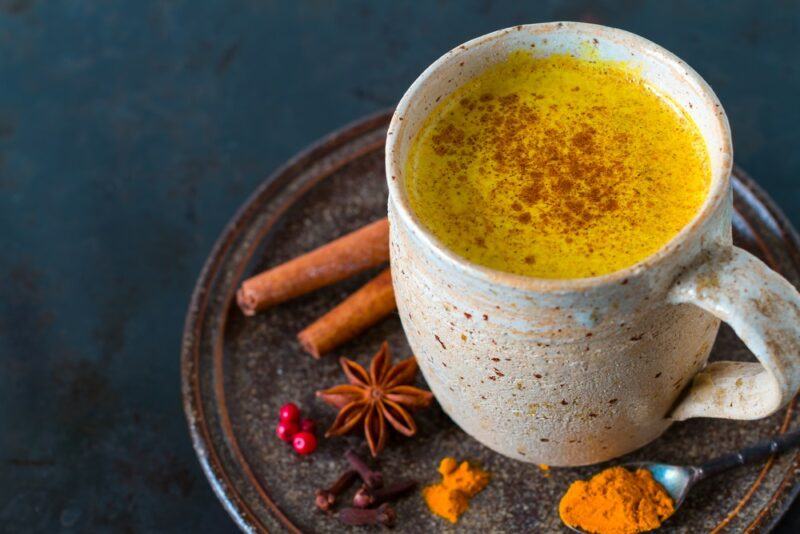 A white mug of turmeric golden milk made with cinnamon, on a dark table