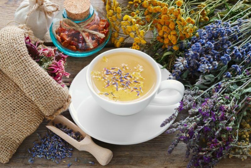 A white mug filled with herbal tea, with many different herbs scattered around it