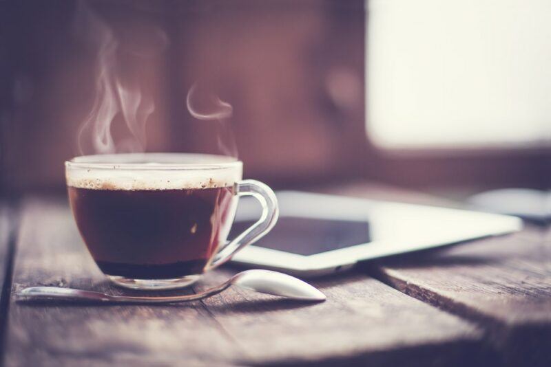 A single mug of coffee on a table, in front of an out of focus window