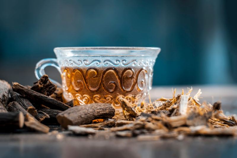 A patterned glass mug containing licorice root tea, with licorice root in front of it