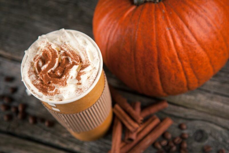 A pumpkin spice latte that's been spiced with Fireball, next to some cinnamon sticks and a full pumpkin