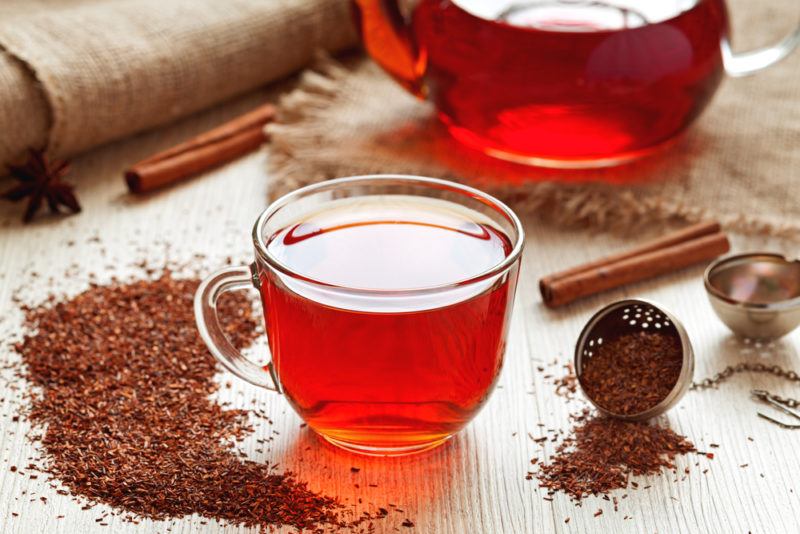 A glass mug and a pot of roobois tea, with powdered roobois on a table