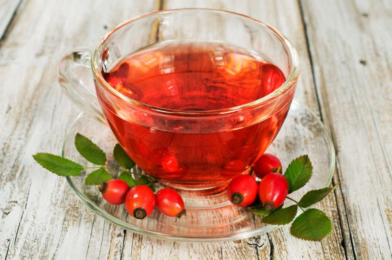 A glass mug of rosehip tea, with a glass saucer that contains rosehips and leaves