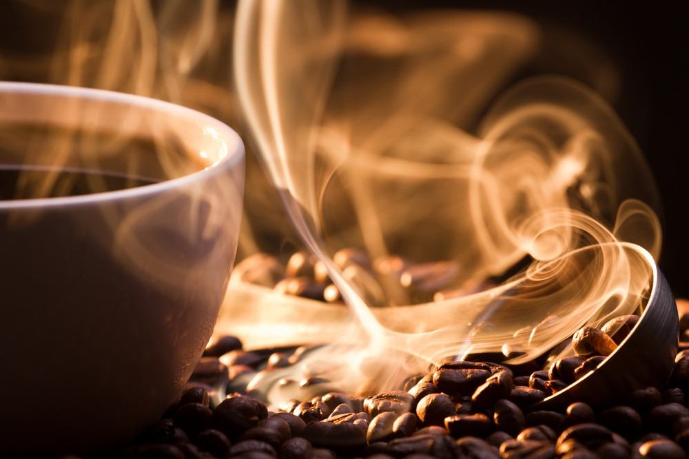 A mug of steaming coffee next to coffee beans