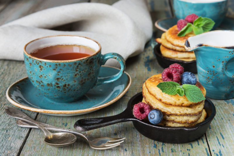 Two small cast iron frypans with stacks of pancakes, next to a mug of tea