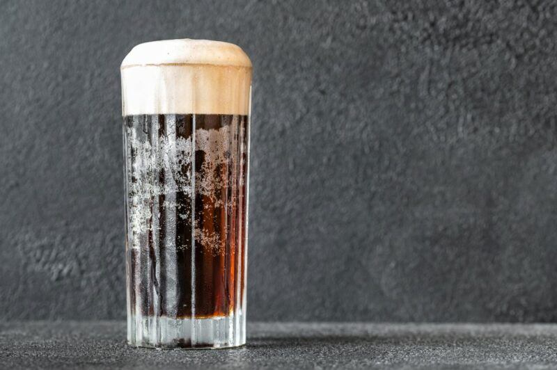 A tall glass containing a newly minted cocktail against a light gray background