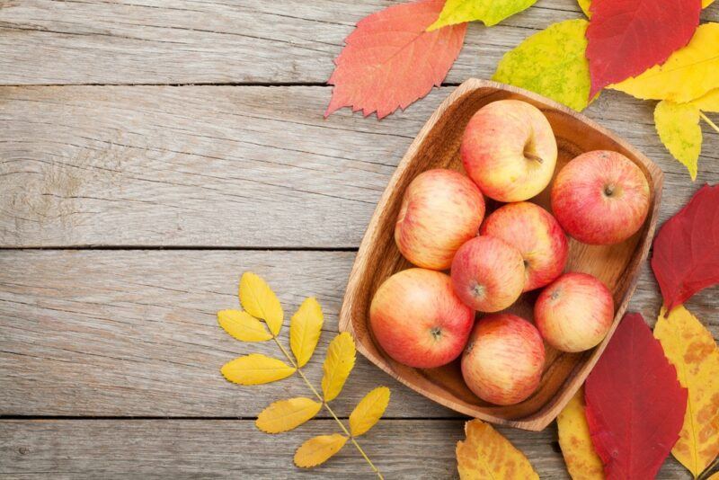 A container of fresh apples next to some fall leaves