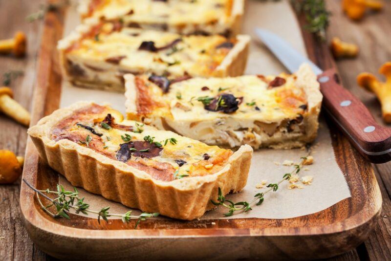 A wooden board with an oblong quiche that has been cut up into pieces