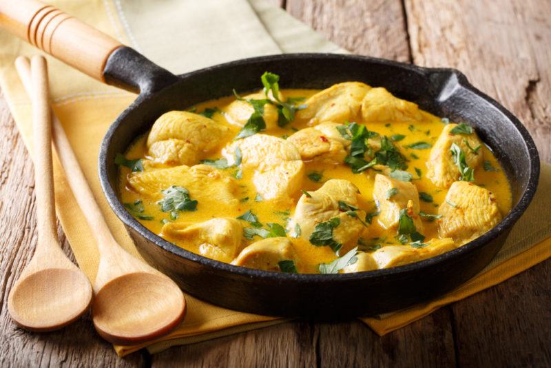 A cast iron pan that contains a coconut chicken stew next to two wooden spoons