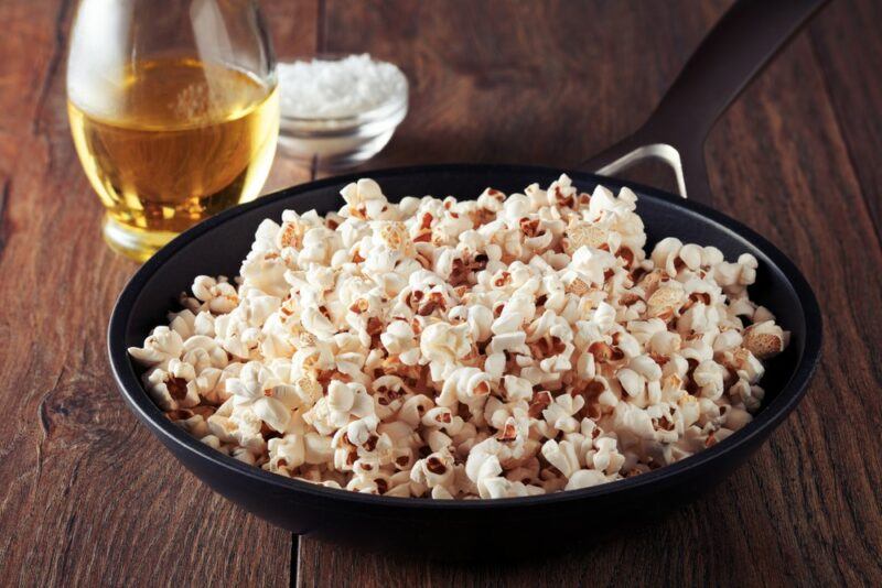 A black pan containing freshly popped popcorn next to olive oil and coconut oi