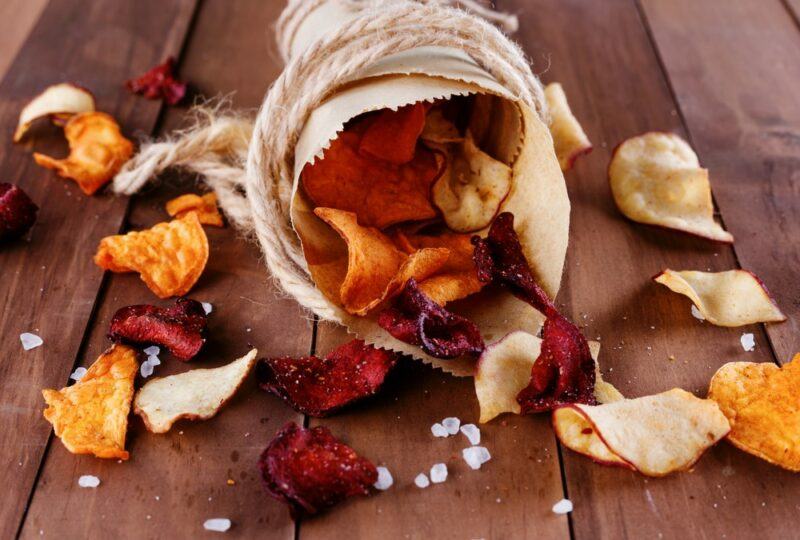 A wooden table with veggie chips in brown paper and string