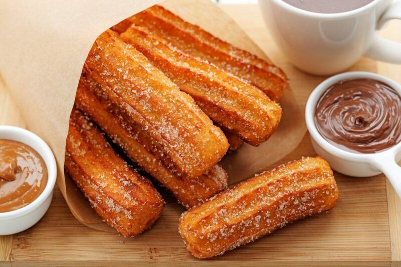 A paper bag with churros, next to chocolate and caramel dips