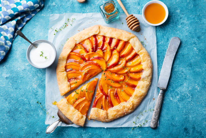 A large peach galette on a table with a piece cut out of it