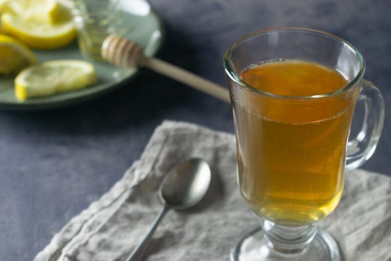 A mug containing a peanut butter hot toddy next to a spoon and lemon pieces