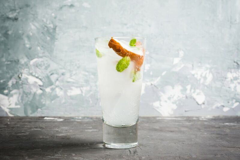 A relatively clear pearl paloma cocktail, garnished with coconut, in front of a wall